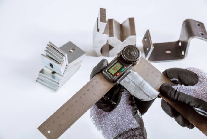 Worker measures the angle of deflection of metal parts on a white background with a protractor.